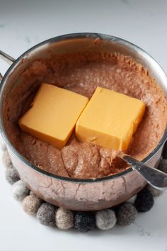 two cubes of butter sit on top of chocolate in a metal bowl with candy balls