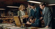 a group of people standing around a table with papers and pencils in front of them