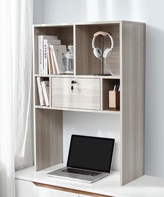 a laptop computer sitting on top of a white desk next to a book shelf filled with books