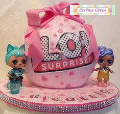 two little dolls are standing next to a large pink cake with the word lol surprise written on it