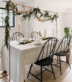 a dining room table with candles and greenery on the top, surrounded by black chairs