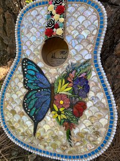 a colorful guitar is sitting on the ground next to a tree and rocks with flowers painted on it