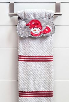 a white towel hanging on the wall with a red santa hat and snowman embroidered on it