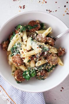 pasta with sausage, spinach and parmesan cheese in a white bowl on a striped napkin