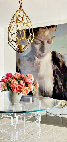 a glass table with flowers on it in front of a large painting and chandelier