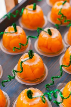 small oranges with green decorations on them in plastic cups, ready to be eaten