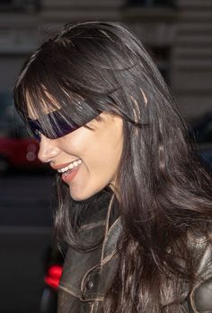 a close up of a person wearing a leather jacket and smiling at something with her hair blowing in the wind