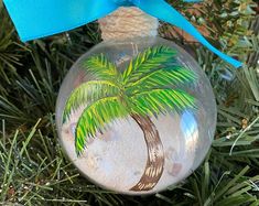 a glass ornament with a palm tree painted on it's side hanging from a christmas tree