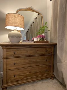 a dresser with a mirror, lamp and flowers on it next to a stair case