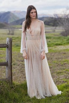 a woman in a long dress standing next to a fence