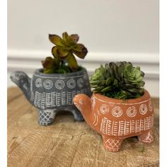 two clay elephants are sitting next to each other on a table with succulents in them