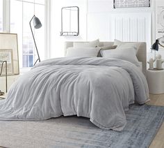 a bedroom with a large bed covered in grey sheets and pillows, next to a window