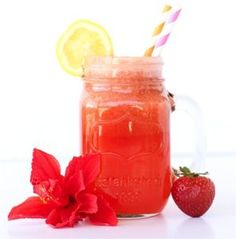 a mason jar filled with liquid next to a red flower and a strawberries on the side