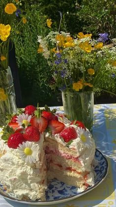 a white cake with strawberries and daisies on a blue and yellow table cloth