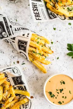 two baskets filled with french fries next to a bowl of dipping sauce and parsley