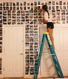 a woman standing on a ladder in front of a wall covered with pictures and photos