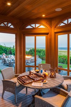 an outdoor dining area with patio furniture and large windows looking out onto the ocean at sunset