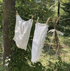 two white shirts hanging on clothesline next to tree in wooded area with green leaves