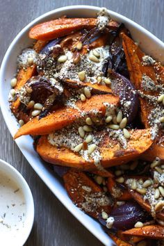 a white bowl filled with roasted carrots next to a cup of yogurt