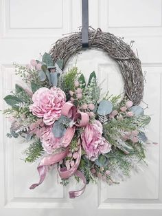 a wreath with pink flowers and greenery hanging on a door