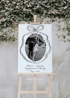 an easel with a photo on it next to a wall covered in greenery