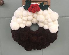 a white and brown wreath hanging on the front door with holly leaves attached to it