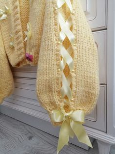 two knitted sweaters with bows hanging from the hooks on a cabinet door handle