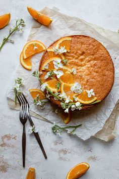 an orange cake with white flowers on top and slices of oranges next to it