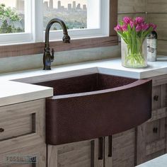 a kitchen sink sitting under a window next to a vase with pink flowers in it