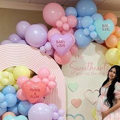 a pregnant woman standing in front of balloons and heart - shaped signs at a baby shower