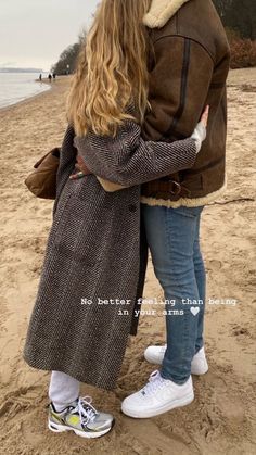 two people standing on the beach hugging each other