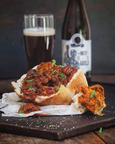 a sandwich with meat and sauce on it next to a glass of beer