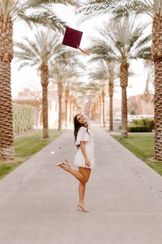 a woman is standing in the middle of a walkway with palm trees and a graduation cap