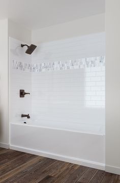 a white bathroom with wood flooring and tiled shower walls, along with an open bathtub