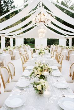 a long table with white plates and place settings is set for an outdoor wedding reception