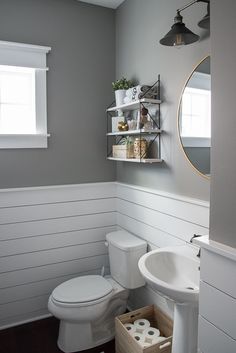 a white toilet sitting next to a sink in a bathroom under a mirror and light fixture