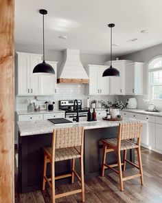 two stools are in front of the kitchen island with white cabinets and black pendant lights