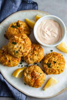 baked crab cakes on a white plate with lemon wedges and dip in the middle