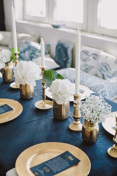 the table is set with gold and blue place settings, white hydrangeas and candles