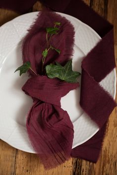 a white plate topped with a purple scarf and a green leaf on top of it