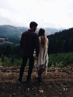 a man and woman standing on top of a mountain looking at the valley below them