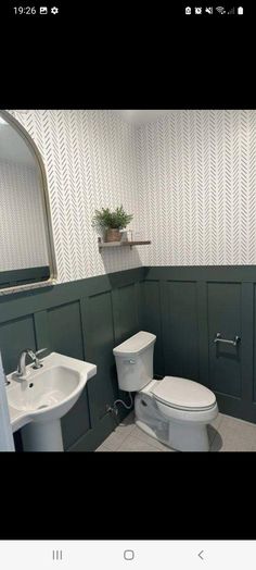 a white toilet sitting next to a sink in a bathroom under a mirror with green paneling on the walls