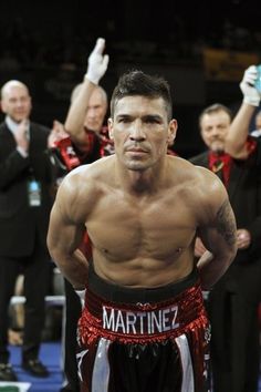 a man with no shirt standing in front of other men wearing red and black trunks