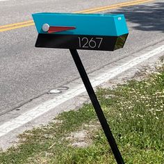 a blue mailbox sitting on the side of a road next to a grass covered field