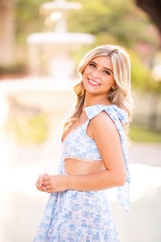 a beautiful young blonde woman in a blue dress smiling at the camera with her hands on her hips