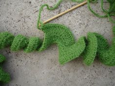 a green crocheted object is laying on the ground next to a knitting needle