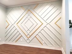 an empty room with wood floors and white walls decorated with gold geometric design on the wall