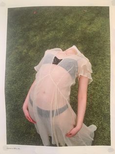 a woman in a sheer dress laying on the grass with her back to the camera