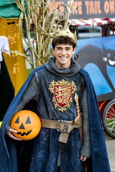 a young boy dressed up as a knight with a pumpkin in his hand and wearing a crown