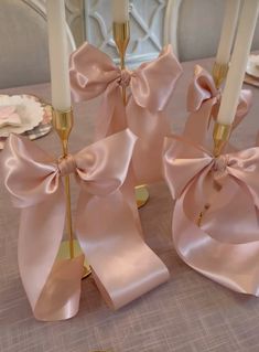 four candles with pink bows on them sitting on a table in front of plates and napkins